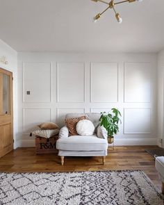 a living room with white walls and wood flooring on the wooden floor, a couch is in front of an area rug that has a potted plant