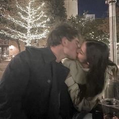 a man kissing a woman on the cheek in front of a building with lights all around