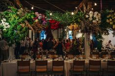 a group of people standing around a long table with flowers hanging from it's ceiling