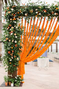 an orange and white wedding arch with flowers on the top, along with greenery