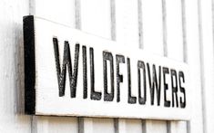 a sign that reads wildflowers on the side of a white building with black lettering