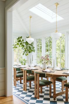 a dining room table with green chairs and a potted plant in the center is surrounded by windows