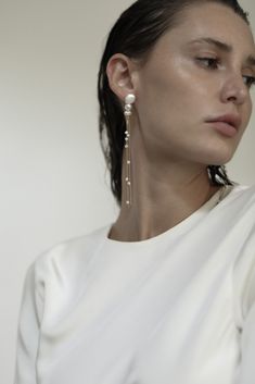 a woman in white shirt with earrings on her head and shoulder, looking off to the side