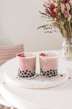 two glasses sitting on top of a white table next to a vase filled with flowers