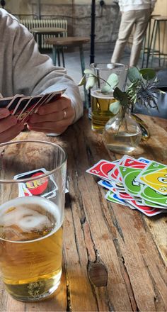 two people sitting at a table with beer and cards on the table next to them