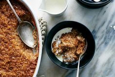 two bowls filled with food on top of a marble counter next to spoons and milk