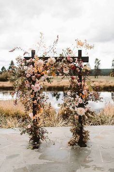 an outdoor ceremony setup with flowers and crosses on the ground next to a pond in front of a cloudy sky