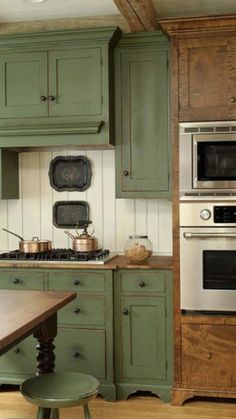 a kitchen with green cabinets and an oven on the wall, along with a wooden dining table