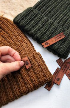 a person is pointing to the cross on top of a knitted beanie hat