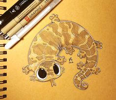 a drawing of a gecko is shown next to some marker pens and a notebook