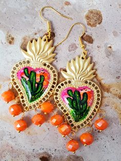 Detailed and beautiful artistically painted earrings, they are painted in detail taking a miniature painting of a cactus in green tones, with a sky in pink, yellow and orange colors, adorned with glass beads, the hooks are hypoallergenic, the earrings are protected with Several layers of high-quality jewelry varnish, improving the quality and durability of the earrings' paint. These earrings are inspired by our Mexican culture and hand painted; They are the ideal gift because they combine with any outfit both day and night, enhancing the beauty of whoever gets them and attracting attention for being unique hand-painted pieces, the Ideal gift for Mother's Day and holidays. Features/ Product info Note: Each earring is hand painted, there are small differences between each pair, so each pair Bohemian Earrings With Artistic Design For Gift, Adjustable Bohemian Earrings With Artistic Design, Artisan Heart Earrings For Pierced Ears As Gift, Artisan Heart Earrings As Gift, Artistic Heart Earrings As Gift, Artsy Orange Jewelry With Matching Earrings, Artistic Heart-shaped Earrings For Gift, Pink Bohemian Hand Painted Jewelry, Artisan Earrings With Artistic Design For Festivals