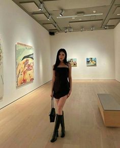 a woman standing in an art gallery holding a handbag and posing for the camera