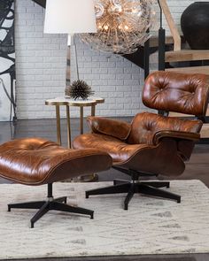 an eames chair and ottoman in front of a brick wall with a chandelier