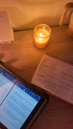 a cell phone sitting on top of a wooden table next to a notebook and candle