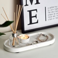 a white tray with candles and rings on it next to a framed print that says me