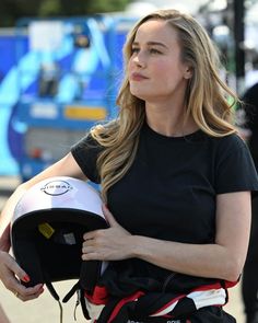 a woman in black shirt holding a helmet on her shoulder and looking off to the side