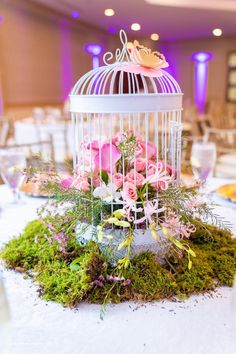 a birdcage filled with pink roses and greenery on top of a table