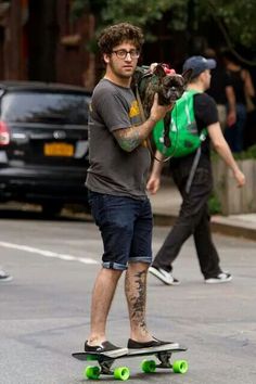 a man riding a skateboard down the street with a dog in his hand and another person walking behind him