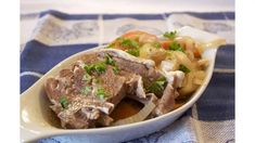 a white bowl filled with meat and vegetables on top of a blue table cloth next to a fork