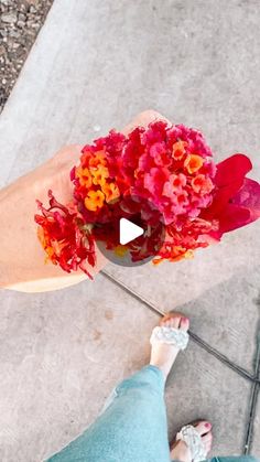 a person standing on the sidewalk with flowers in their hand and a video screen showing them