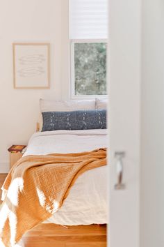 a bed sitting under a window next to a wooden floor in a room with white walls