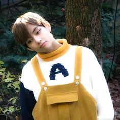 a young man wearing a backpack standing in front of a tree