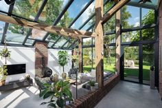 a living room filled with furniture and lots of windows next to a brick wall covered in plants