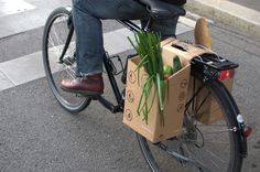 a person riding a bike with a box on the back filled with green onions and carrots