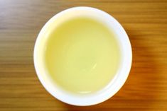 a small white bowl sitting on top of a wooden table next to a cup filled with liquid