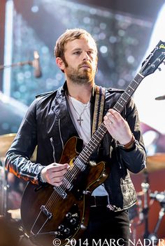 a man with a beard playing an electric guitar on stage at a music festival or concert