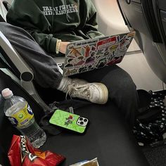 a man sitting on an airplane with his feet propped up and reading a newspaper, surrounded by other items