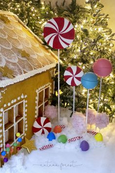 a gingerbread house with candy and lollipops in the snow next to a christmas tree