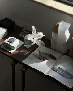 an open book sitting on top of a wooden table next to a vase with flowers