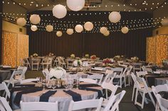 tables and chairs are set up for an event with paper lanterns hanging from the ceiling