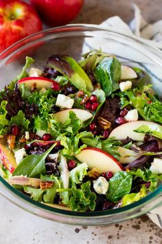 a salad with apples and cheese in a glass bowl on a table next to an apple