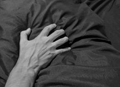 black and white photograph of person's hand resting on the back of a bed