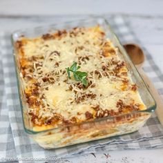 a casserole dish with meat and cheese on top is sitting on a checkered tablecloth