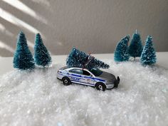 a toy police car is parked in the snow next to small christmas trees that are blue and white