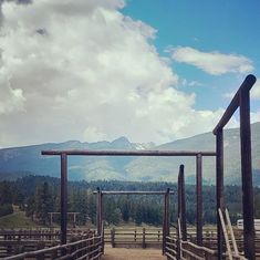 a wooden fenced in area with mountains in the back ground and clouds in the sky