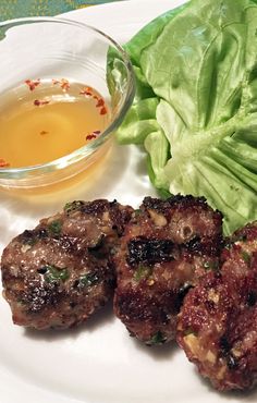 some meat patties and lettuce on a plate next to a bowl of dressing