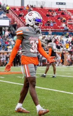 a football player wearing an orange and gray uniform walking on the field with his hands in his pockets