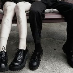 two people sitting on a bench with their legs crossed and one person wearing black shoes