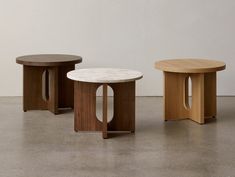 three wooden tables sitting next to each other on top of a cement floor in front of a white wall