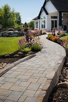 a brick walkway leading to a house with flowers in the front yard and landscaping around it