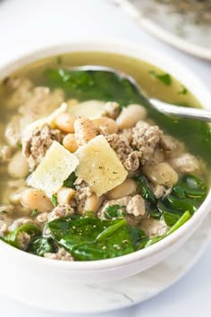 a bowl of soup with spinach, meat and potatoes in it on a table