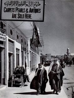 two men are walking down the street in front of some shops with signs above them