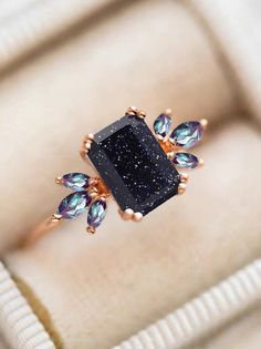 a black diamond ring sitting on top of a white velvet cushioned box with blue and green crystals