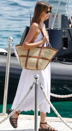 a woman in a white dress is holding a brown bag and standing on a dock