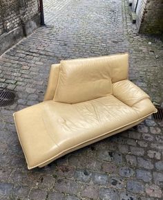 a tan leather couch sitting on top of a cobblestone street