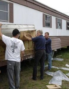 three men standing next to a trailer in front of a house with siding on it